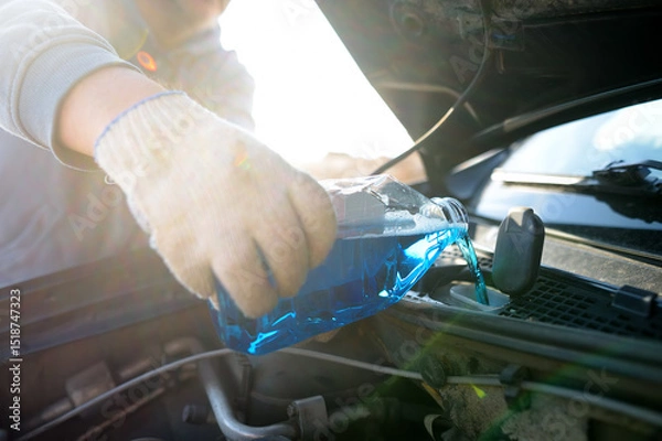 Fototapeta Man auto mechanic pours the liquid for washing the windows of the car