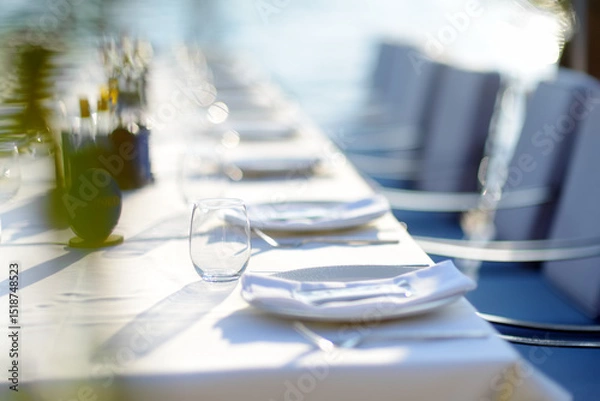 Fototapeta A row of empty plates on a long table with a white tablecloth. A table in a Mediterranean restaurant ready to serve a large group of visitors or tourists.