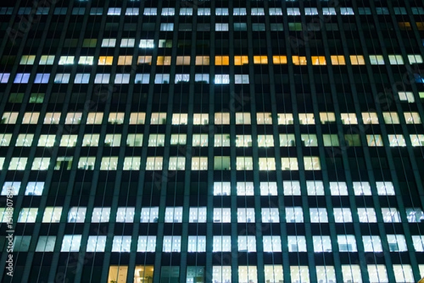 Fototapeta Tokyo, Japan, panoramic view of the facade of an office building at night with lights on in most windows of offices where people work