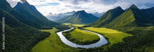 Fototapeta Aerial view of a green valley framed by towering mountain peaks, with a winding river reflecting the sky