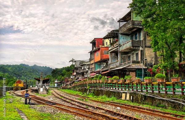 Fototapeta Colorful hillside houses overlook the curving railway tracks and a small diesel locomotive at Shifen Station on the Pingxi line in New Taipei, Taiwan, with lush forested hills beneath a cloudy summer