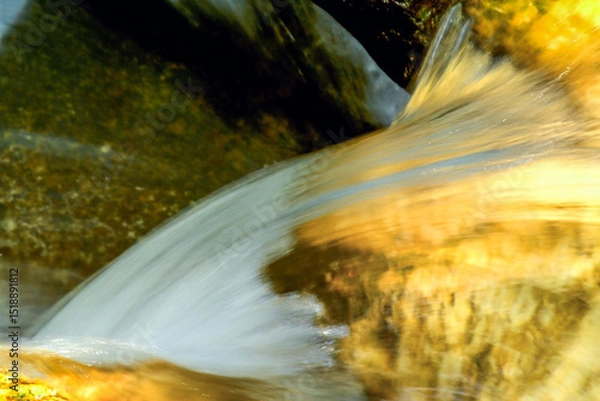 Fototapeta Close-up of clear water cascading over golden-hued rocks at Qing Shan Waterfall, Taiwan, creating a smooth, ethereal effect.