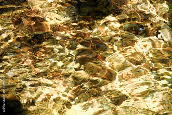 Obraz Close-up abstract of sunlight reflecting on rippled clear water revealing a golden-hued riverbed at Qing Shan Waterfall, Taiwan.