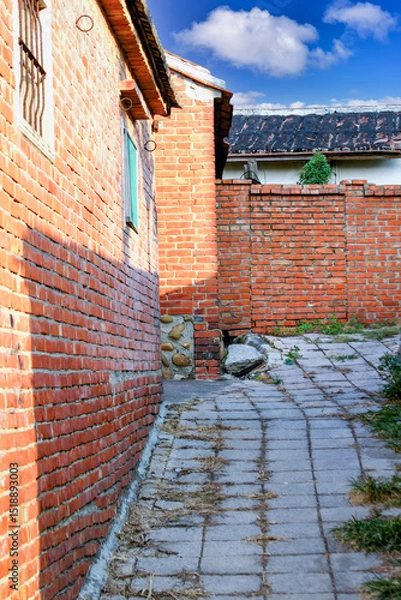 Obraz A view of a narrow alleyway with aged red brick walls in Houlong Port, Miaoli County, Taiwan. The ground is paved with stone tiles.
