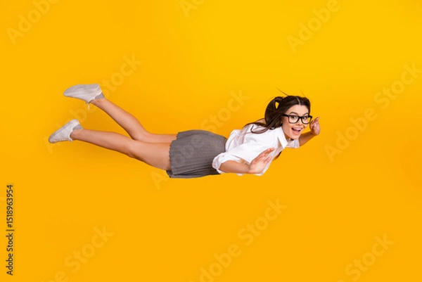 Fototapeta Cheerful young woman poses joyfully as if flying, expressing happiness and fun in a playful and dynamic yellow studio setting