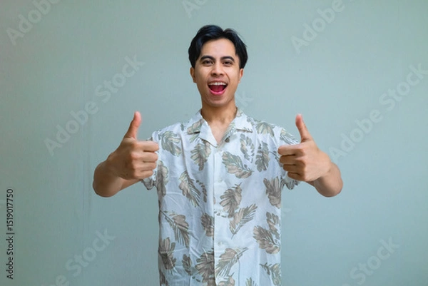 Fototapeta Happy young Asian man in summer clothes smiling and giving two thumbs up to the camera, expressing excitement and positivity, isolated on a clear background