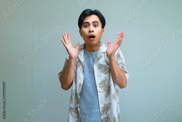 Fototapeta Portrait of a young Asian man in summer clothes with a shocked facial expression, looking directly at the camera against a clear background, perfect for surprise or reaction concepts