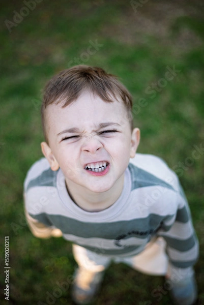 Fototapeta Portrait of a young boy looking up and smiling playfully at the camera 