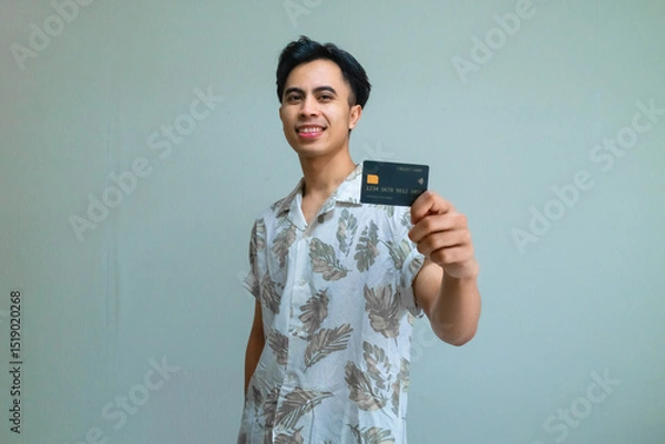 Fototapeta Portrait of a smiling young Asian man in summer clothes showing a card product, perfect for advertisement with a clear background
