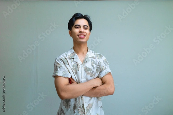 Fototapeta Portrait of a confident young Asian man smiling with arms crossed, wearing casual summer clothes, standing against a clear background, showing positive and relaxed energy