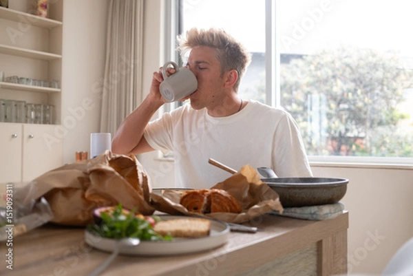 Fototapeta oung man drinking coffee while having breakfast at home