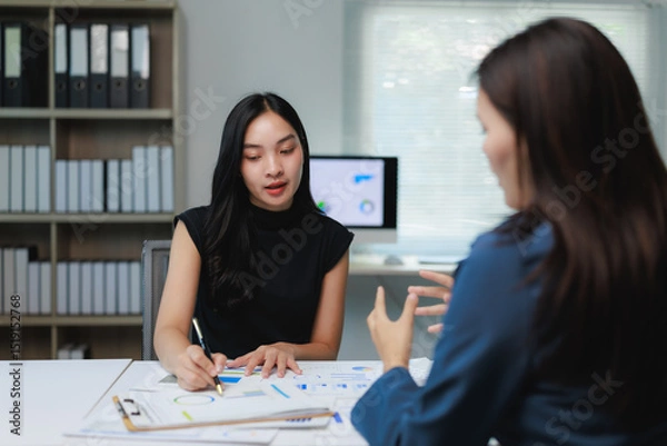 Fototapeta Two businesswomen discussing charts and analyzing statistics in office meeting