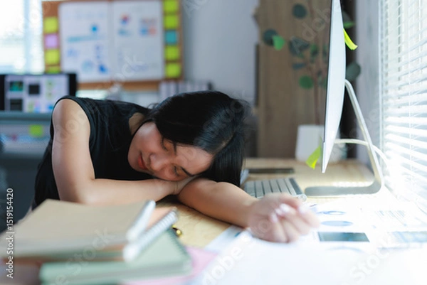 Fototapeta Exhausted asian freelancer sleeping at her desk after working long hours