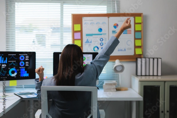 Fototapeta Businesswoman celebrating success while working with financial charts on computer in office