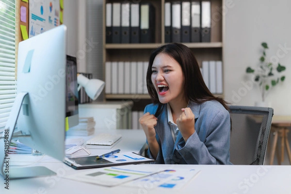Fototapeta Excited businesswoman celebrating success while working on computer in office