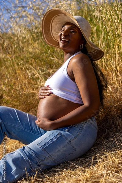 Obraz A joyful and radiant pregnant woman is seen relaxing outdoors, fully embracing the stunning beauty of nature while eagerly anticipating the arrival of motherhood during the warm summer months ahead