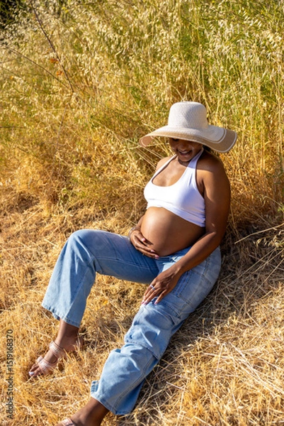 Obraz A serene pregnant woman enjoys a tranquil moment outdoors, showcasing her baby bump and embracing love and connection during warm summer days, reflecting a joyful bond with her baby