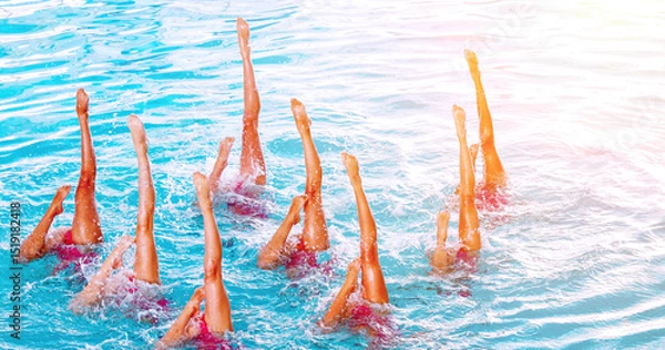 Fototapeta Synchro swimmers perform an elegant routine in a bright blue pool under the sun