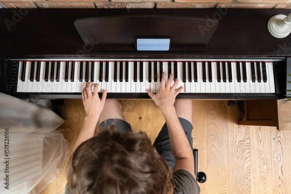 Fototapeta A musician plays a digital piano, seen from a top-down perspective. A smartphone with a learning app rests on the music stand, illustrating online music education or a modern hobby.