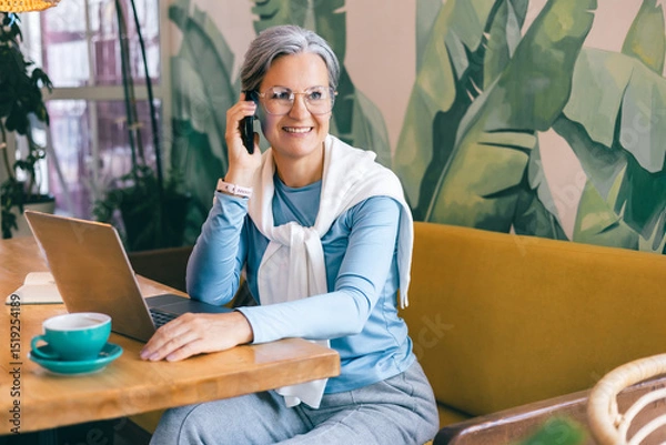 Fototapeta Thoughtful senior freelancer woman taking a break from laptop in a stylish modern cafe setting