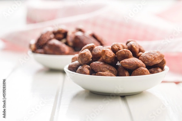 Fototapeta Almond nuts coated in sugar and honey in bowl on white table.