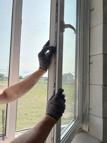 Fototapeta A worker adjusts a plastic window in a new country house. Installing plastic windows in a new building.