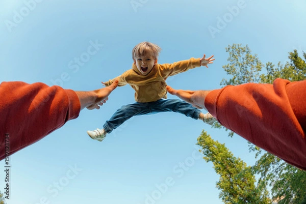 Obraz POV view, father tosses high and catches his excited joyful son. Energetic young boy with arms outstretched flying midair against a blue sky, thrown by parent during playful outdoor moment. 