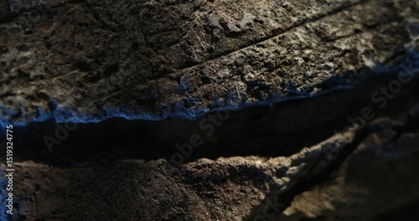 Fototapeta Close-up of layered rock with deep cracks and blue-toned lighting effects