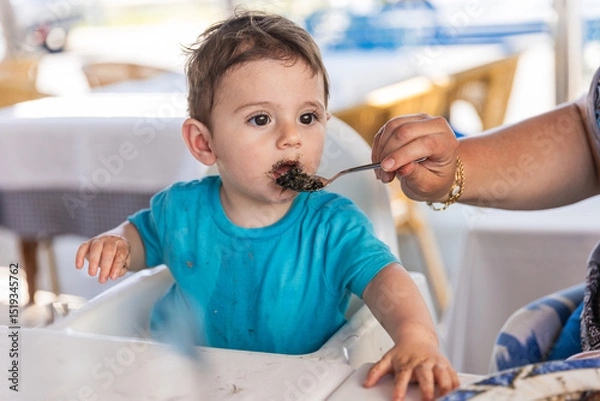 Fototapeta Grandmother feeding one year old grandson with black rice cooked with squid ink