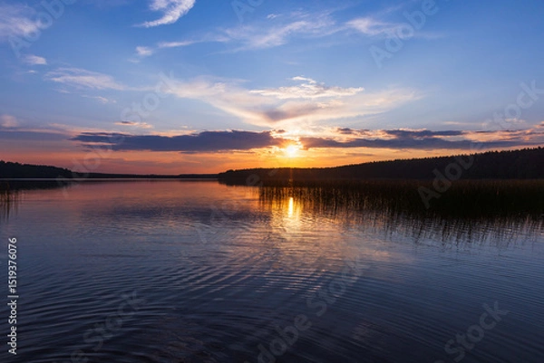 Obraz Tranquil sunset view over a calm lake with reflections of the plants and forest