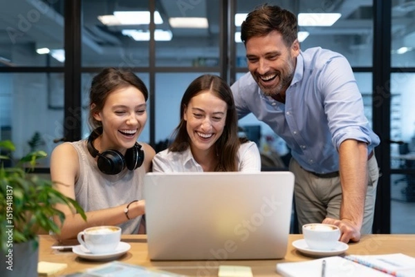 Fototapeta Three cheerful coworkers enjoying a moment of success while looking at a laptop in a modern office setting with coffee cups on the table