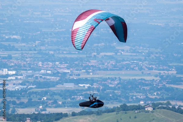 Obraz Sestola, Italy – 05 31 2025: Paraglider flies in the air. Aerial view of paragliding. Paraglider flies above the mountains in a bright sunny day. Concept of extreme sport.
