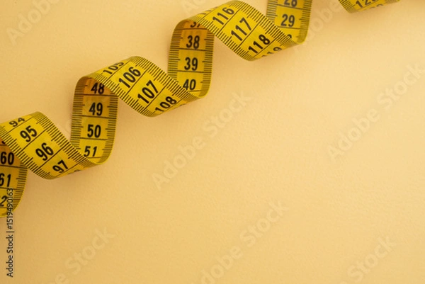 Fototapeta Yellow measuring tape on a yellow background. Tool for measuring length and volume. Tape for measuring in the clothing industry or the volume of the human body