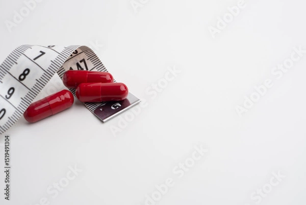 Fototapeta Measuring tape and tablets, vitamins on a light background with space for text. Concept of losing weight, dieting, burning fat, healthy eating.  