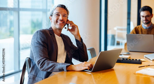 Fototapeta Confident professional man talking on the phone in office with laptop