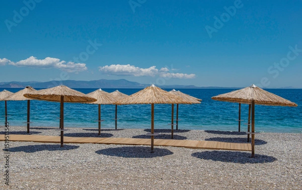 Fototapeta straw umbrella on a beach of white pebbles n Peloponnese, Greece with their well drawn shadow in front beautiful sea