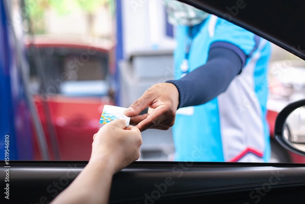 Fototapeta Showing a hand extending a credit card to a gas station attendant for payment. This image captures the typical scene of fuel purchase, highlighting convenience and modern payment methods at the pump.