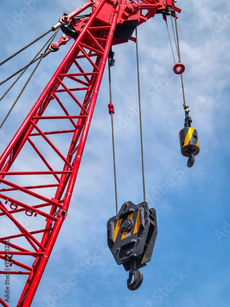 Obraz Heavy crane with pulleys lifting materials against a blue sky at a construction site