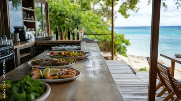 Obraz Long wooden table with two plates of food on it. the table is set up on a wooden deck overlooking the ocean. the ocean is visible in the background, with turquoise water and white sand.