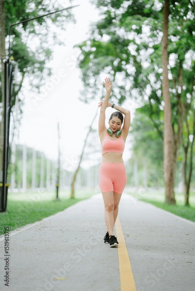 Obraz Beautiful Asian woman is exercising and running alone in a village park, happy and smiling in the morning.