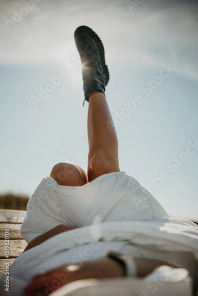 Fototapeta Woman wrapped in blanket and wearing black boots lies on a wooden bench with her legs up in the air