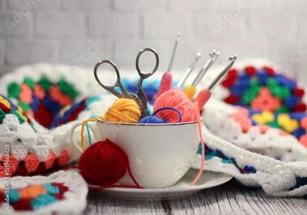 Fototapeta A cup and a saucer with clews balls of yarn wool and crocheted blanket handmade craft bright photo	