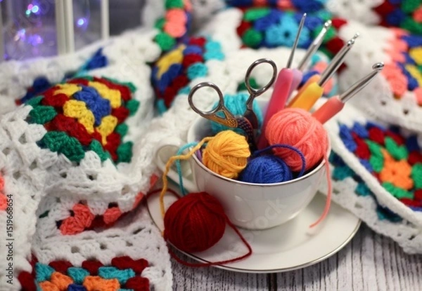 Fototapeta A cup and a saucer with clews balls of yarn wool and crocheted blanket handmade craft bright photo	