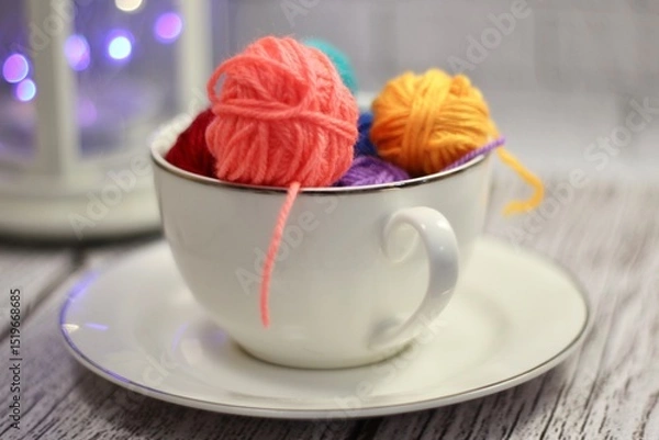 Fototapeta A cup and a saucer with clews balls of yarn wool and crocheted blanket handmade craft bright photo	