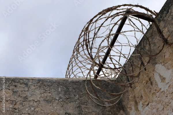 Fototapeta High sandstone prison wall, with razor wire on top, dark moody sky. Background concept. Copy space. Crime, felony, legal system, conviction rate, justice, sentencing, escapees. Youth crime statistics.