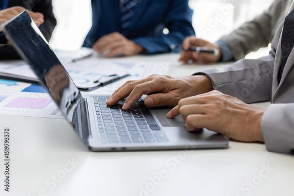 Obraz Businessman analyzing financial chart and report using laptop computer. Business people working together at office desk analyzing financial charts and reports using laptop.