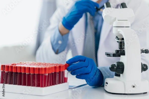 Obraz Scientist analyzing blood sample using microscope in laboratory. Scientist in gloves examines a blood sample under a microscope in a lab, discovering medical mysteries.