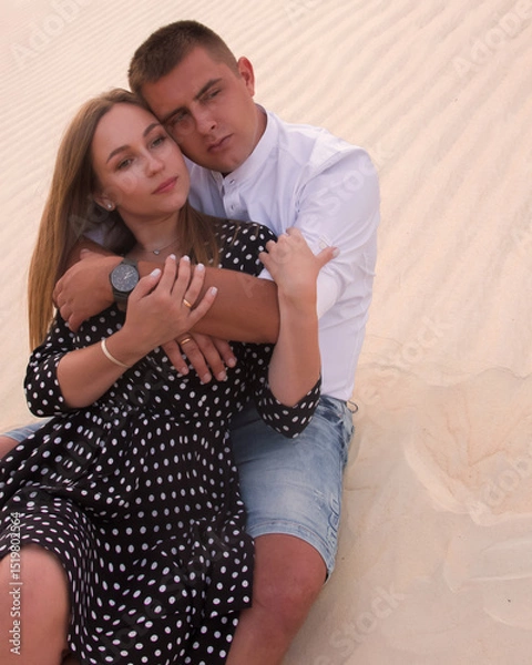 Fototapeta romantic couple relationship. man and woman are sitting casual on a sand dunes career background in hugs and looking away with smile in desert at sunset. lifestyle concept, free space