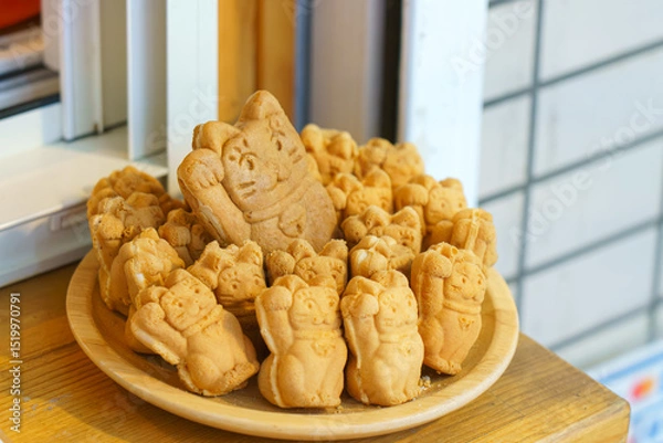 Fototapeta Tokyo, Japan - Sep 30 2024, A close-up view of a bowl filled with Taiyaki pies in the form of a Maneki Neko, in the window of a cafe, Tokyo, Japan