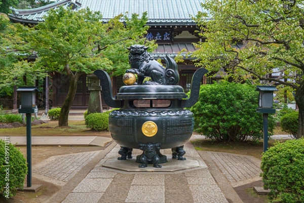 Fototapeta Tokyo, Japan - Sep 30 2024, Panoramic view of the bronze incense burner decorated with a lion statue, surrounded by trees, on road to Gotokuji Temple, without people, at daytime, Tokyo, Japan